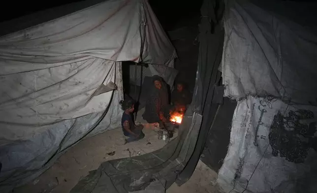 Shireen Daifallah, who was displaced with her children from northern Gaza, checks the fire next to their tent at a camp for displaced people in Deir al-Balah. Gaza Strip, Saturday, Nov. 30, 2024. (AP Photo/Abdel Kareem Hana)