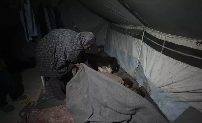 Shireen Daifallah, who was displaced from northern Gaza, checks one of her children in their tent at a camp for displaced people in Deir al-Balah. Gaza Strip, Saturday, Nov. 30, 2024. (AP Photo/Abdel Kareem Hana)