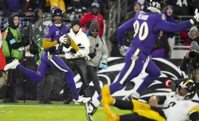 Pittsburgh Steelers quarterback Russell Wilson, bottom right, hits the turf as Baltimore Ravens cornerback Marlon Humphrey, left, returns an interception for a touchdown during the second half of an NFL football game, Saturday, Dec. 21, 2024, in Baltimore. (AP Photo/Stephanie Scarbrough)