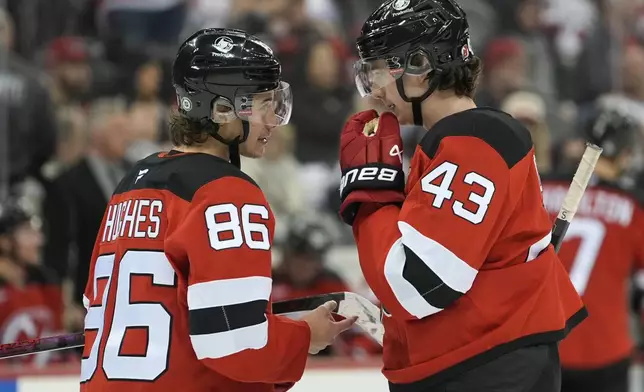 New Jersey Devils' Jack Hughes, left, and Luke Hughes, right, talk during the third period of an NHL hockey game against the Washington Capitals, Saturday, Nov. 30, 2024, in Newark, N.J. (AP Photo/Pamela Smith)