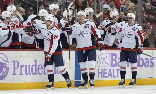 Washington Capitals' Connor McMichael, left, Tom Wilson, center, and Pierre-Luc Dubois, right, celebrate after McMichael scored during the second period of an NHL hockey game against the New Jersey Devils, Saturday, Nov. 30, 2024, in Newark, N.J. (AP Photo/Pamela Smith)