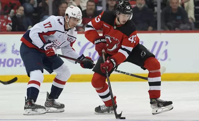 New Jersey Devils' Luke Hughes, right, skates with the puck against Washington Capitals' Dylan Strome, left, during the first period of an NHL hockey game Saturday, Nov. 30, 2024, in Newark, N.J. (AP Photo/Pamela Smith)