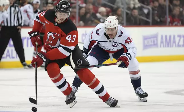 New Jersey Devils' Luke Hughes, left, skates with the puck against Washington Capitals' Tom Wilson, right, during the third period of an NHL hockey game Saturday, Nov. 30, 2024, in Newark, N.J. (AP Photo/Pamela Smith)