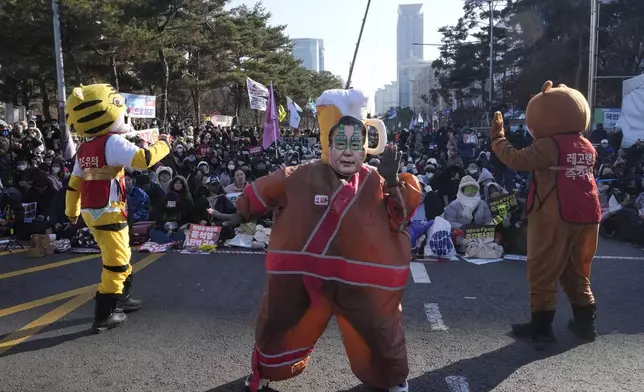 A participant, center, wearing a mask of South Korean President Yoon Suk Yeol performs before a rally to demand his impeachment outside the National Assembly in Seoul, South Korea, Saturday, Dec. 14, 2024. (AP Photo/Ahn Young-joon)