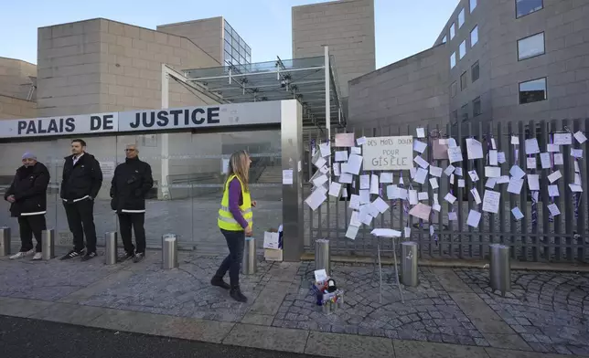 A woman walks past poster attached on the fence of the Palace of Justice during a women's rights demonstration, Saturday, Dec. 14, 2024 in Avignon, southern France, where the trial of dozens of men accused of raping Gisèle Pelicot while she was drugged and rendered unconscious by her husband is taking place. (AP Photo/Aurelien Morissard)