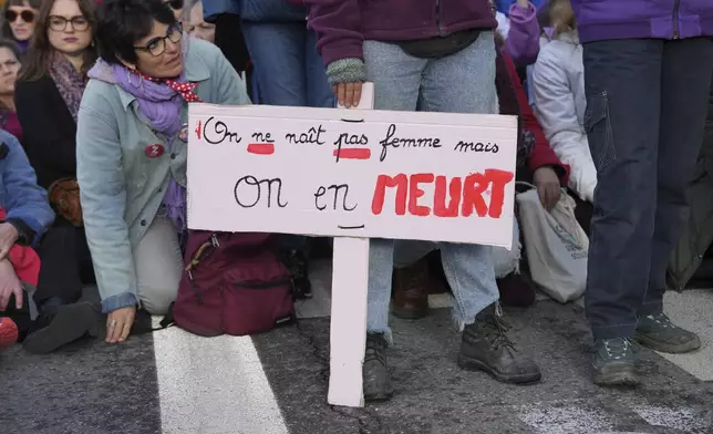 A woman sits by a placard reading " We are not born a woman but we die of it" during a women's rights demonstration, Saturday, Dec. 14, 2024 in Avignon, southern France, where the trial of dozens of men accused of raping Gisèle Pelicot while she was drugged and rendered unconscious by her husband is taking place. (AP Photo/Aurelien Morissard)