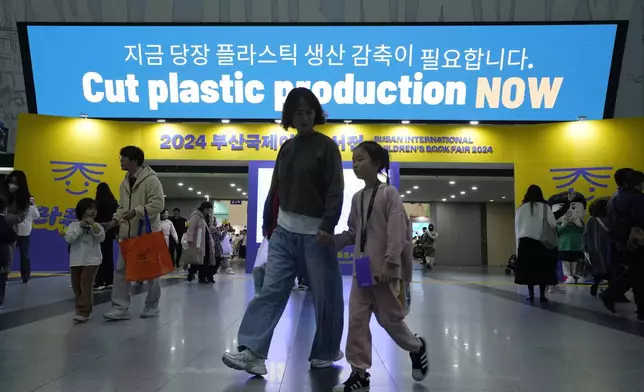 FILE - People pass by a sign calling for a reduction in plastic production near the venue for the fifth session of the Intergovernmental Negotiating Committee on Plastic Pollution in Busan, South Korea, Nov. 30, 2024. (AP Photo/Ahn Young-joon)