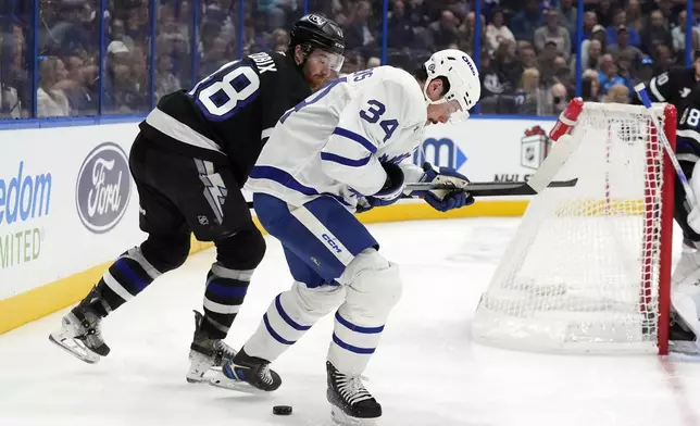 Toronto Maple Leafs center Auston Matthews (34) battles with Tampa Bay Lightning defenseman Nick Perbix (48) for the puck during the first period of an NHL hockey game Saturday, Nov. 30, 2024, in Tampa, Fla. (AP Photo/Chris O'Meara)