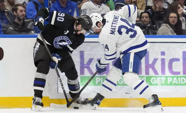 Tampa Bay Lightning defenseman J.J. Moser (90) and Toronto Maple Leafs center Auston Matthews (34) battle for the puck during the first period of an NHL hockey game Saturday, Nov. 30, 2024, in Tampa, Fla. (AP Photo/Chris O'Meara)