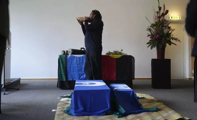 Yessie Mosby from Ugar Island in Australia blows the shell behind coffins, during a ceremony for the return of Aboriginal Australians ancestors to their relatives and communities at the Ethnological Museum in Berlin, Germany, Thursday, Dec. 5, 2024. (AP Photo/Markus Schreiber)