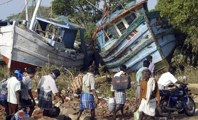 Villagers walk with their belongings past two boats that were washed ashore by tidal waves at Nagappattinam, in the southern Indian state of Tamil Nadu, Dec. 28, 2004. (AP Photo/Gautam Singh, File)