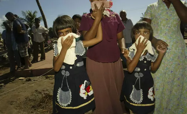 Twin girls hold towels to their faces to fend off the smell of decomposing bodies lying on streets in Hambantota, southern Sri Lanka Thursday Dec. 30, 2004. (AP Photo/Elizabeth Dalziel, File)