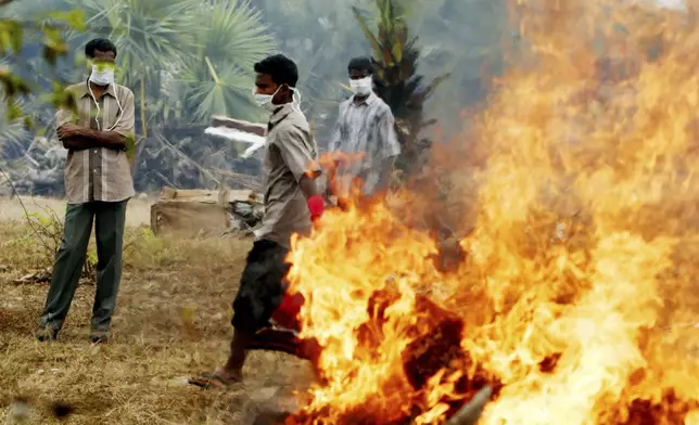 Workers, searching for bodies remaining unburied in Mullaitivu following Sunday's tsunami which completely destroyed the village, walk away from a fire which they started to burn the bodies of two victims Friday, Dec. 31, 2004. (AP Photo/Ed Wray, File)