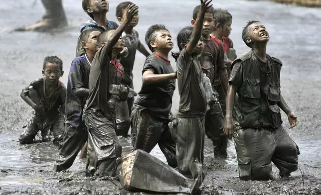 Refugee children try to catch relief goods tossed from an Australian military helicopter in a rice paddy in Lampaya, outskirts of Banda Aceh, Indonesia, Jan. 17, 2005. (AP Photo/Eugene Hoshiko, File)