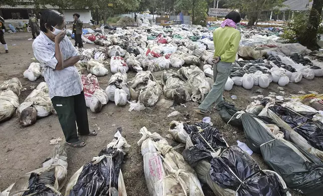 Thais walk outside a Buddhist temple where more than 1,000 bodies have been gathered, near Takuapa, Thailand, Thursday, Dec. 30, 2004. (AP Photo/David Longstreath, File)