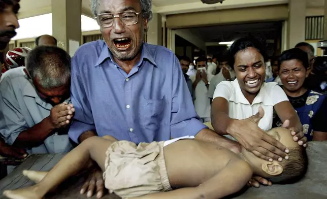 A young tsunami victim's father cries along with other family members as he holds the body of his son at the hospital in Galle, Sri Lanka, Dec. 27, 2004. (AP Photo/Vincent Thian, File)