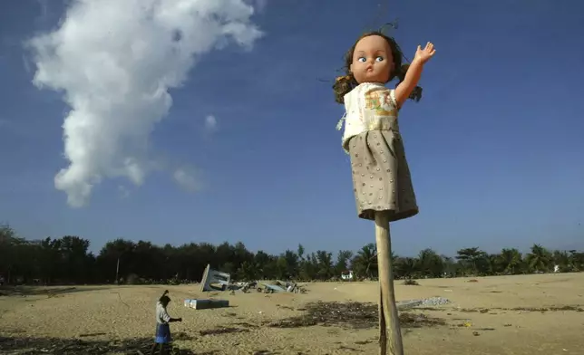 A doll is erected on pole by a family in memory of their child who was killed by the Dec. 26, 2004 tsunami, as a survivor works, background, at Cheddi Palayan, about 230 kilometers (144 miles) east of Colombo, Sri Lanka, Monday, Jan. 31, 2005. (AP Photo/Rafiq Maqbool, File)