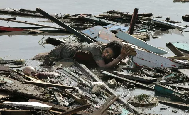 An Acehnese woman clings to floating debris while being swept by a tsunami Sunday, Dec. 26, 2004 in Banda Aceh, the capital of Aceh province in northwest Indonesia. A man tried to rescue her but both victims were swept by the current and died as witnessed by the photographer. (AP Photo/Frans Dellian, File)