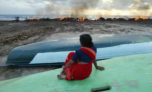 Sitting on a boat, a woman watches debris of destroyed homes being burned at the fishermen's village in Nagappattinam, in the southern Indian state of Tamil Nadu, Monday Jan. 3, 2005. (AP Photo/Saurabh Das, File)