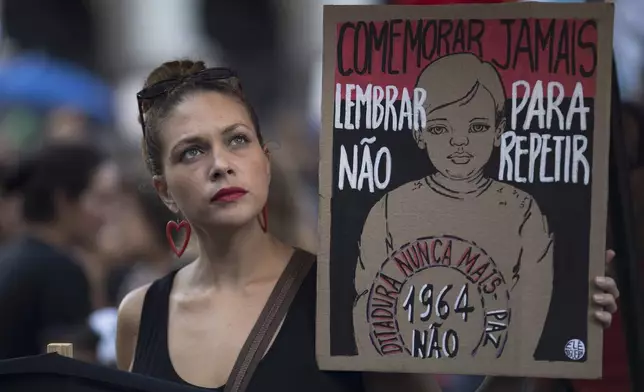 FILE - A demonstrator holds a sign that reads in Portuguese "Never commemorate. Remember in order to not repeat. Dictatorship never again," during a protest against Brazil's 1964 military coup, in Rio de Janeiro, March 31, 2019. (AP Photo/Leo Correa, File)