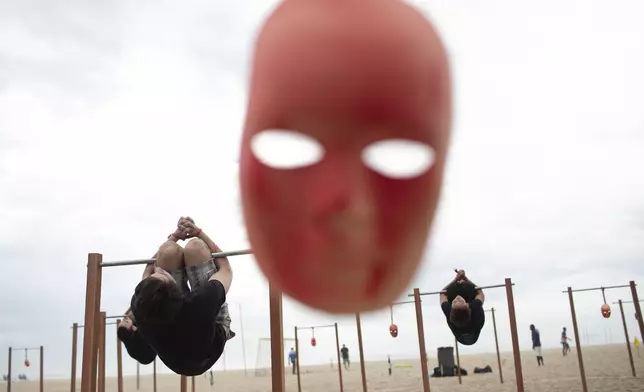 FILE - With a mask hanging in the foreground, demonstrators perform as victims in a torture device called pau-de-arara, or parrot's perch, during a demonstration organized by the Rio de Paz NGO to remember the victims of Brazil's military dictatorship, on Copacabana beach in Rio de Janeiro, Dec. 10, 2019. (AP Photo/Silvia Izquierdo, File)