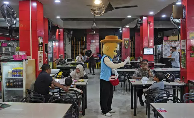 A street busker gestures as he talks to a guests at a coffee shop in Banda Aceh, Indonesia, Friday, Dec. 13, 2024. (AP Photo/Achmad Ibrahim)