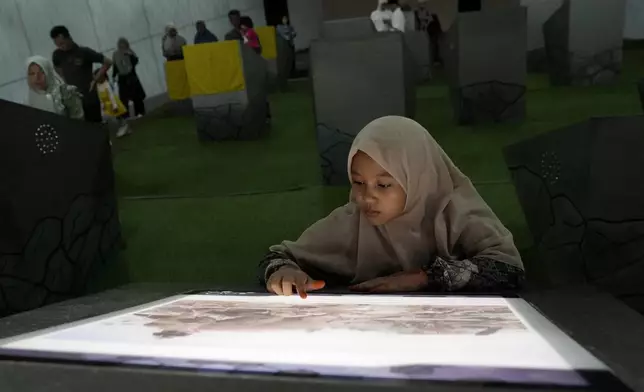 A young girl looks at a photo displayed at the Tsunami Museum in Banda Aceh, Indonesia, Saturday, Dec 14, 2024. (AP Photo/Achmad Ibrahim)