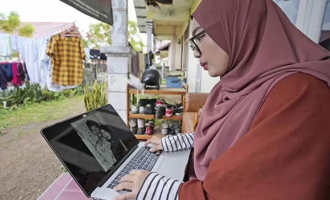 Qurrata Ayuni, a 28-year-old tsunami survivor, looks at the photo of her parents who were killed during the disaster, in Banda Aceh, Indonesia, Friday, Dec. 13, 2024. (AP Photo/Achmad Ibrahim)