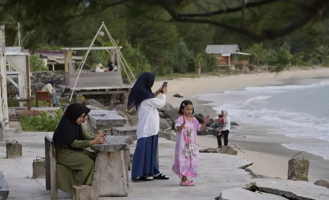 Young girls use their mobile phones as they visit Lampuuk beach, one of the areas hardest hit by Indian Ocean tsunami in 2004, on the outskirts of Banda Aceh, Indonesia, Friday, Dec. 13, 2024. (AP Photo/Achmad Ibrahim)