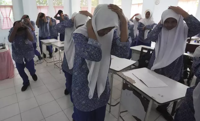 Students cover their head during an earthquake drill at a school in Banda Aceh, Indonesia, Thursday, Dec. 12, 2024. (AP Photo/Achmad Ibrahim)