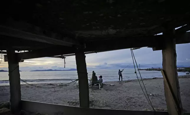 A man fishes as his family looks on in Banda Aceh, Indonesia, Wednesday, Dec. 11, 2024. (AP Photo/Achmad Ibrahim)