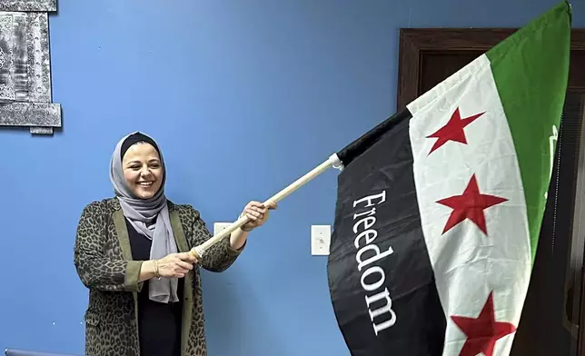 Rama Alhoussaini holds a Syrian flag in her Dearborn Heights, Mich., office, Tuesday, Dec. 10, 2024. (AP Photo/Corey Williams)