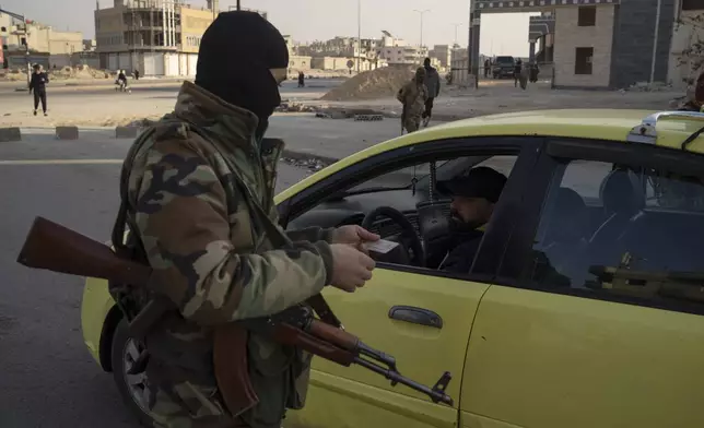 A member of the security forces of the newly formed Syrian government checks the ID of a driver at a security checkpoint in Homs, Syria, Thursday, Dec. 26, 2024. (AP Photo/Leo Correa)