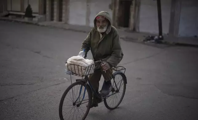 An elderly man transports a plastic bag with bread as he rides his bicycle on a street in an Alawite neighbourhood, in Homs, Syria, Thursday, Dec. 26, 2024. (AP Photo/Leo Correa)