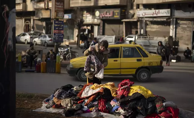 A women looks at second hand clothes displayed on a street for sale near an Alawite neighbourhood, in Homs, Syria, Thursday, Dec. 26, 2024. (AP Photo/Leo Correa)