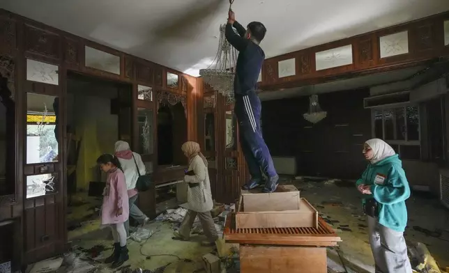 A man tries to take a chandelier as people search for belongings in the ransacked private residence of Syrian President Bashar Assad in the Malkeh district of Damascus, Syria, on Sunday, Dec. 8, 2024. (AP Photo/Hussein Malla)