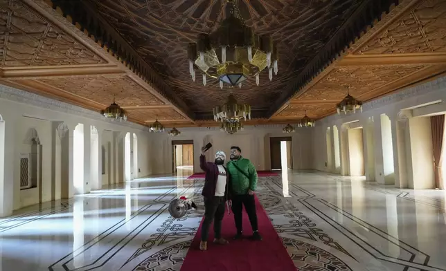 Two men use their cell phones while walking through the halls of Syrian President Bashar Assad's presidential palace in Damascus, Syria, Sunday, Dec. 8, 2024. (AP Photo/Hussein Malla)