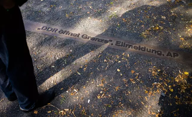 FILE -In this Sept. 4, 2019 photo Frieder Reimold the former Berlin bureau chief of The Associated Press' German service casts his shadow on the ground at a remembrance plug with the AP news alert "DDR oeffnet Grenze," or "East Germany opens border" during an interview with the Associated Press in Berlin, Germany. On Nov. 9, 1989. (AP Photo/Markus Schreiber, File)