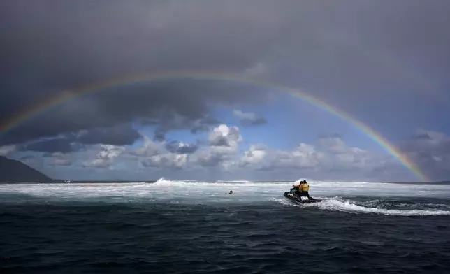 Members of the water safety team move into the impact zone on a jet ski to rescue a surfer under a rainbow during a training day ahead of the 2024 Summer Olympics surfing competition in Teahupo'o, Tahiti, on July 23, 2024. (AP Photo/Gregory Bull)