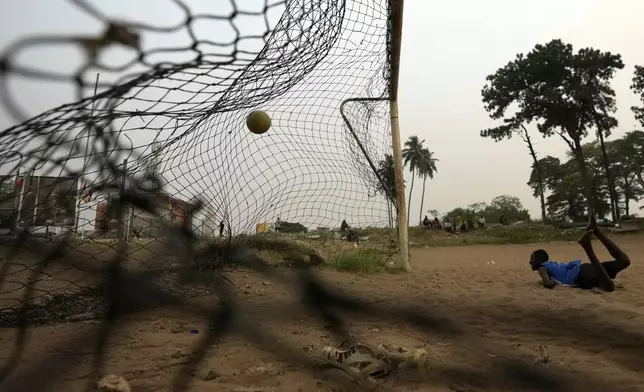 A young man watches the ball after diving while playing soccer on a dusty field in Abidjan, Ivory Coast, on Feb. 6, 2024. (AP Photo/Themba Hadebe)