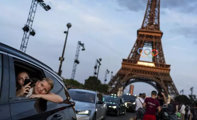 Passengers in the back of a taxi film themselves as they leave the Eiffel Tower, decorated with the Olympic rings ahead of the 2024 Summer Olympics, in Paris, on July 17, 2024. (AP Photo/David Goldman)