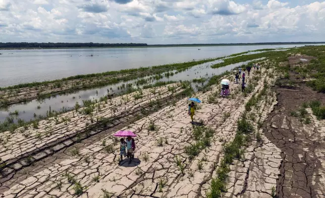 People walk through a part of the Amazon River that shows signs of drought in Santa Sofia, on the outskirts of Leticia, Colombia, on Oct. 20, 2024. (AP Photo/Ivan Valencia)