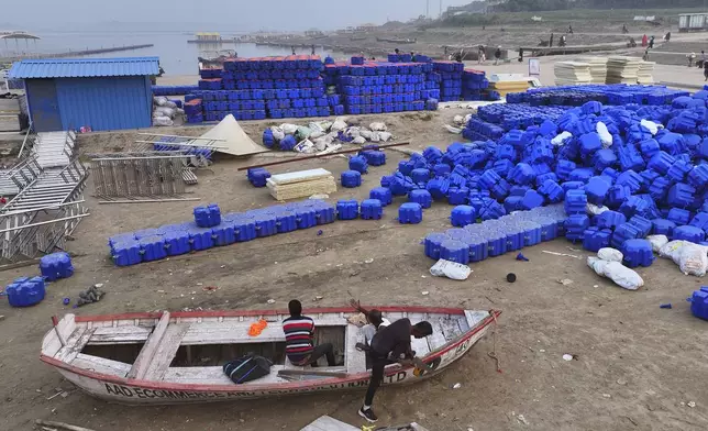 Workers repair a boat next to a pile of interlocking plastic cubes meant for building a floating jetty on the Ganges river in preparation for the upcoming Maha Kumbh Mela, one of the world's largest religious festivals, in Prayagraj, India, Saturday, Nov. 30, 2024. (AP Photo/Rajesh Kumar Singh)