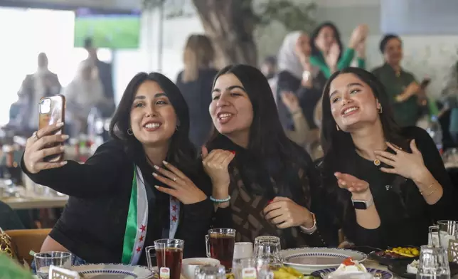 FILE - A Syrian woman with a scarf in colors of the Syrian opposition flag takes a selfie with her friends as they celebrate in a restaurant in Damascus, Syria, Tuesday, Dec. 17, 2024. (AP Photo/Omar Sanadiki, File)