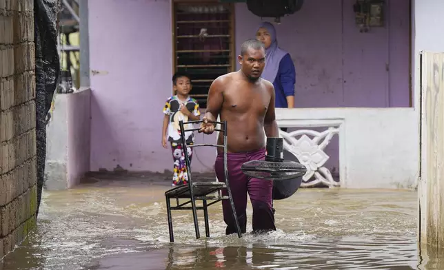 A man removes a chair and a fan from his flooded house in Tumpat, Malaysia, Tuesday, Dec. 3, 2024. (AP Photo/Vincent Thian)