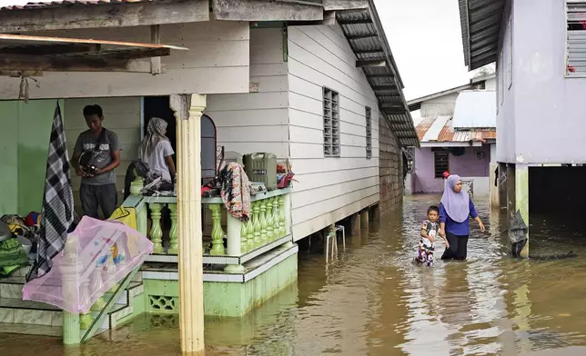 People wade through the water at a neighborhood affected by a flood in Tumpat, on the outskirts of Kota Bahru, Malaysia, Tuesday, Dec. 3, 2024. (AP Photo/Vincent Thian)