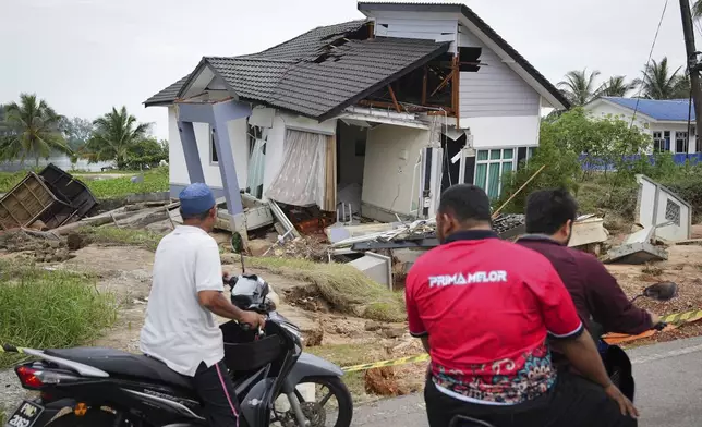 Motorists survey a house damaged by a flood in Tumpat, on the outskirts of Kota Bahru, Malaysia, Tuesday, Dec. 3, 2024. (AP Photo/Vincent Thian)