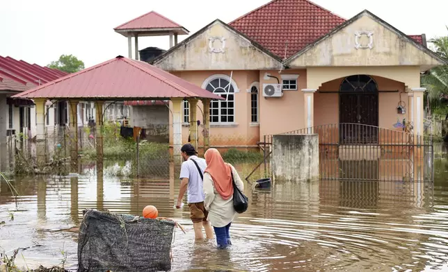 People wade through the water at a neighborhood affected by a flood in Tumpat, on the outskirts of Kota Bahru, Malaysia, Tuesday, Dec. 3, 2024. (AP Photo/Vincent Thian)