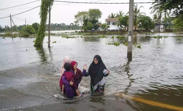 People wade through flood waters in Tumpat, outskirts of Kota Bahru, Malaysia, Tuesday, Dec. 3, 2024. (AP Photo/Vincent Thian)