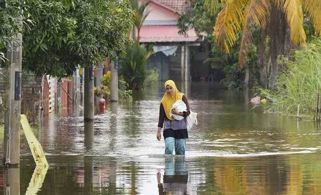 A woman wades through floodwater in Tumpat, on the outskirts of Kota Bahru in Kelantan state on the east coast of Malaysia, Tuesday, Dec. 3, 2024. (AP Photo/Vincent Thian)